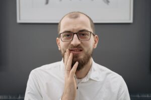 Homem com expressão de dor segurando o rosto por causa de dor de dente